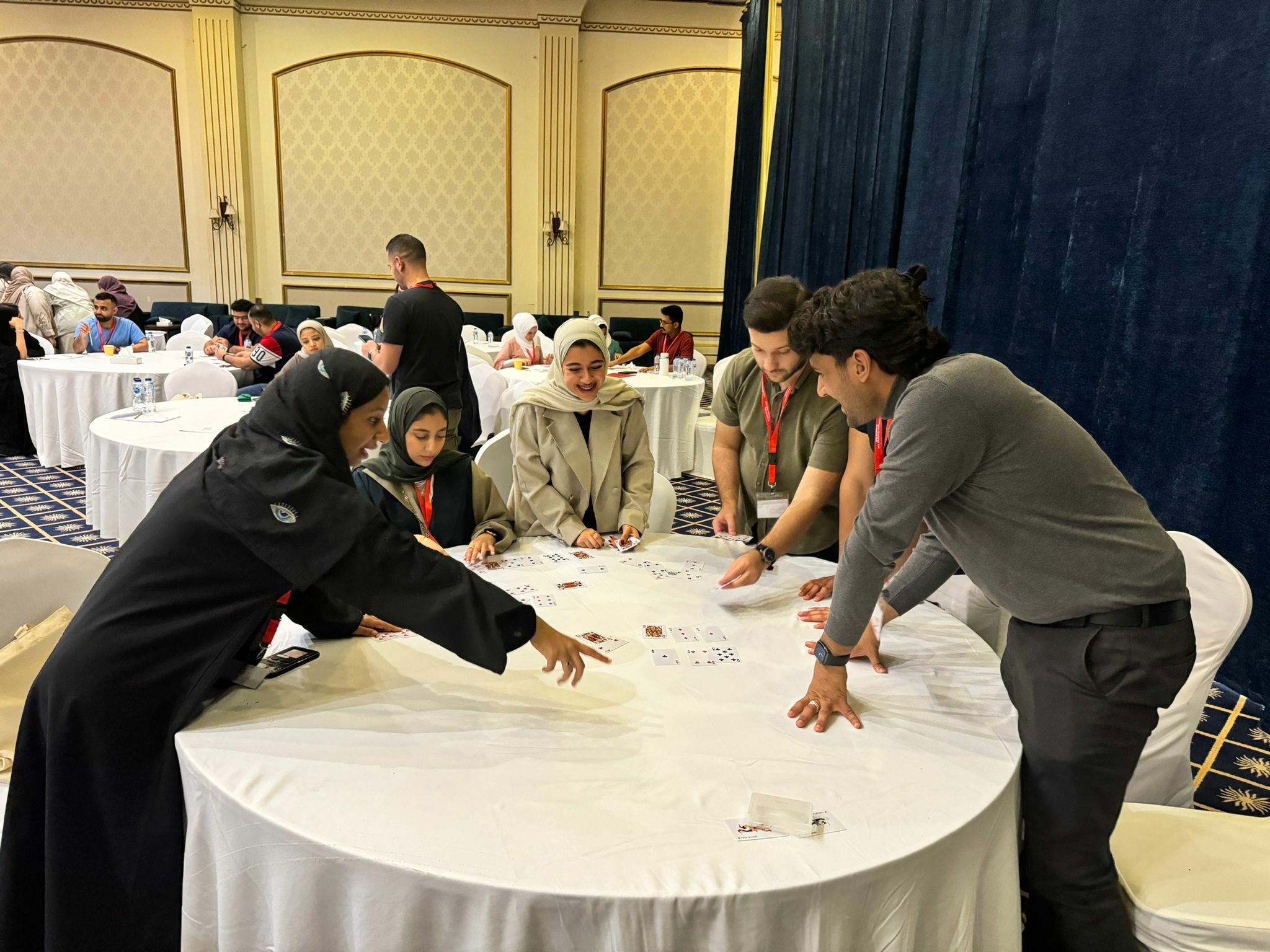 People around a table engaged in an activity with cards, wearing lanyards, in a decorated conference room.