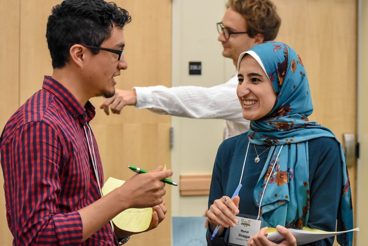 Guy in red shirt talking to woman in blue headscarf and shirt.